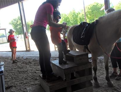 Woman helping child walk up steps to get on a horse